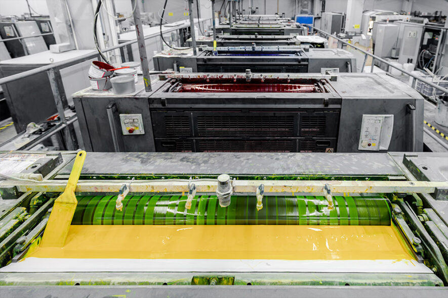 the top of a printing machine with yellow ink rolling into the machine